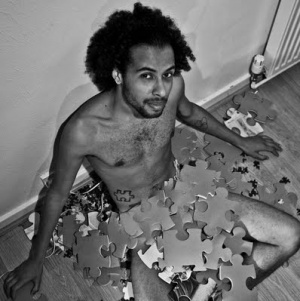 Atta sitting naked on the floor partly covered by large jigsaw puzzle pieces